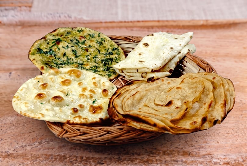 Woven basket filled with assorted Indian flatbreads, including naan, paratha, and roti.