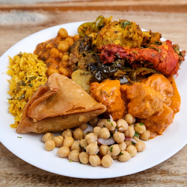 Colorful Indian platter with yellow rice, samosa, chicken tikka, butter chicken, and chickpea curry.