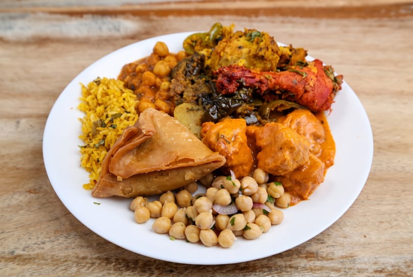 Colorful Indian platter with yellow rice, samosa, chicken tikka, butter chicken, and chickpea curry.