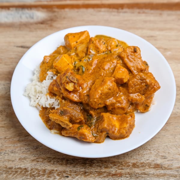 Plate of orange curry with white rice on a wooden table.