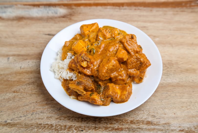 Plate of orange curry with white rice on a wooden table.