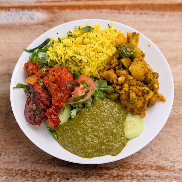 Colorful Indian thali with yellow rice, red chicken, green chutney, and potato curry on wood.