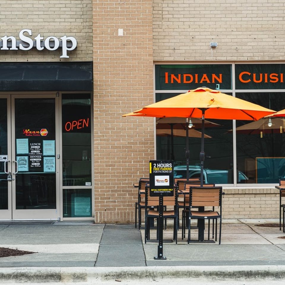 NaanStop Indian Cuisine storefront with outdoor seating, orange umbrellas, and a red inflatable tube man.