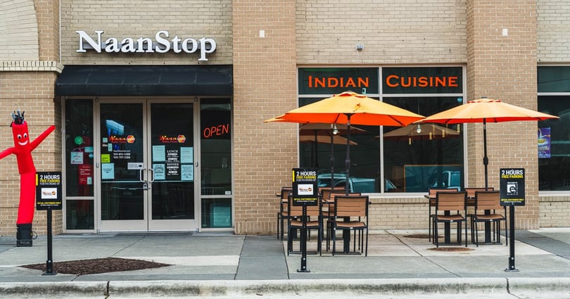 NaanStop Indian Cuisine storefront with outdoor seating, orange umbrellas, and a red inflatable tube man.