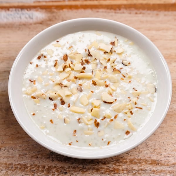 Creamy white dish topped with chopped almonds in a white bowl on a wooden table.