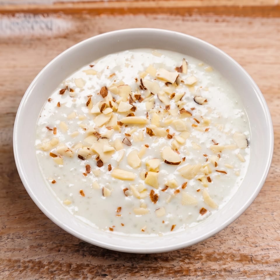 Creamy white dish topped with chopped almonds in a white bowl on a wooden table.