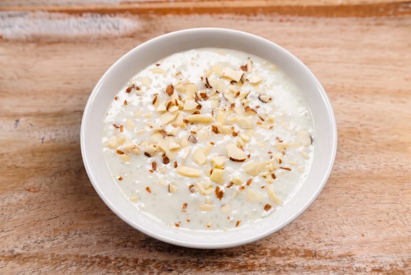 Creamy white dish topped with chopped almonds in a white bowl on a wooden table.