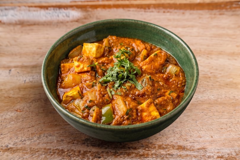Vibrant paneer curry with onions, bell peppers, and fresh cilantro in a green bowl.