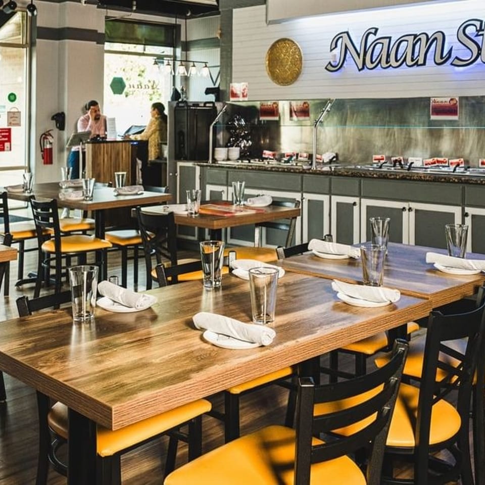 Bright Naan Stop restaurant interior with set tables, yellow chairs, and a long buffet.