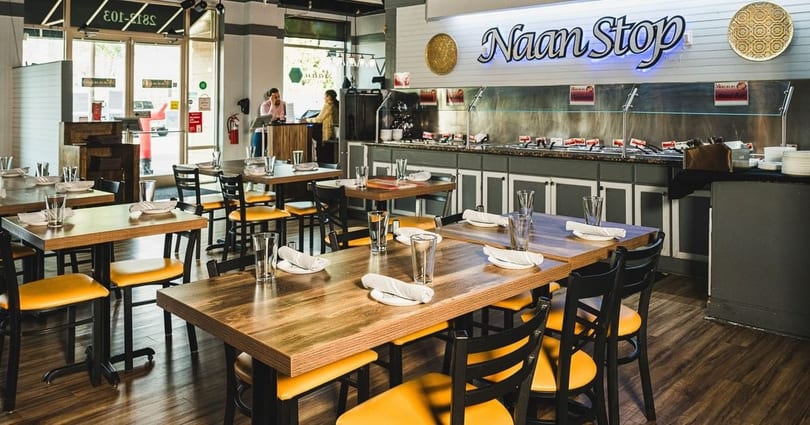 Bright Naan Stop restaurant interior with set tables, yellow chairs, and a long buffet.